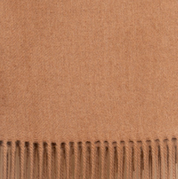 Camel colored baby alpaca throw blanket styled on leather chair in warm-toned living room