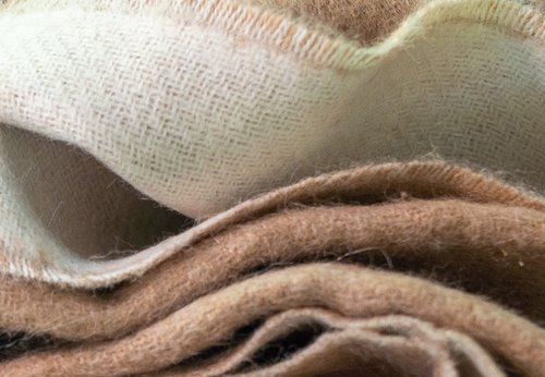 Close-up of the ELEMENTA Cielo reversible throw blanket, showing its ivory and beige baby alpaca sides