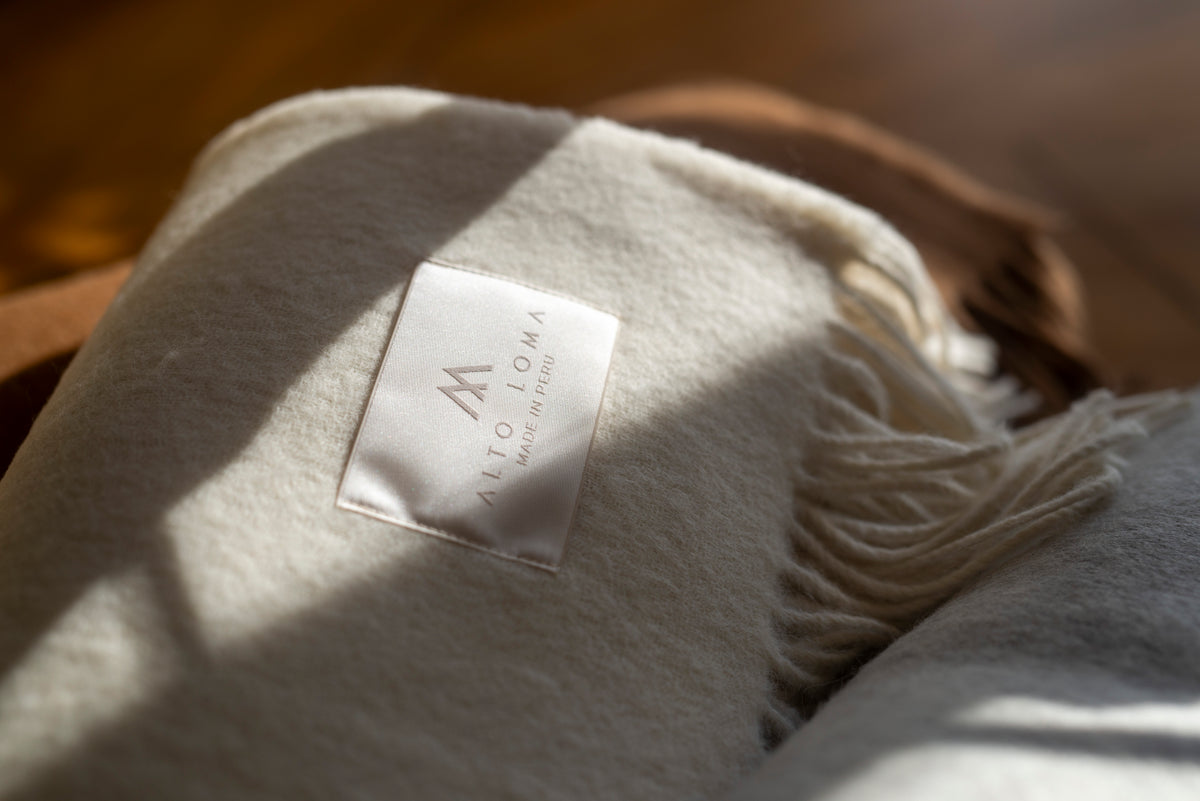 Folded ivory Maras baby alpaca throw blanket with the ALTO LOMA label, lit by afternoon sun