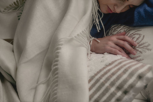 Woman asleep beneath the ivory Maras baby alpaca throw blanket, its fringe falling across her hand