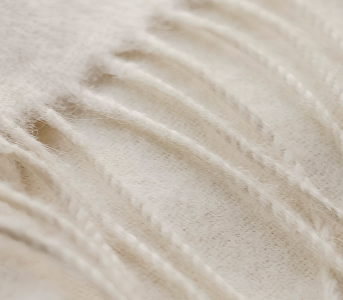 Close-up of the ELEMENTA Maras throw blanket in ivory baby alpaca, showing its soft surface and twisted fringe