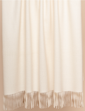 Ivory baby alpaca throw blanket draped over bed in airy neutral bedroom setting
