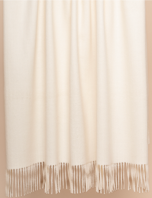 Ivory baby alpaca throw blanket draped over bed in airy neutral bedroom setting